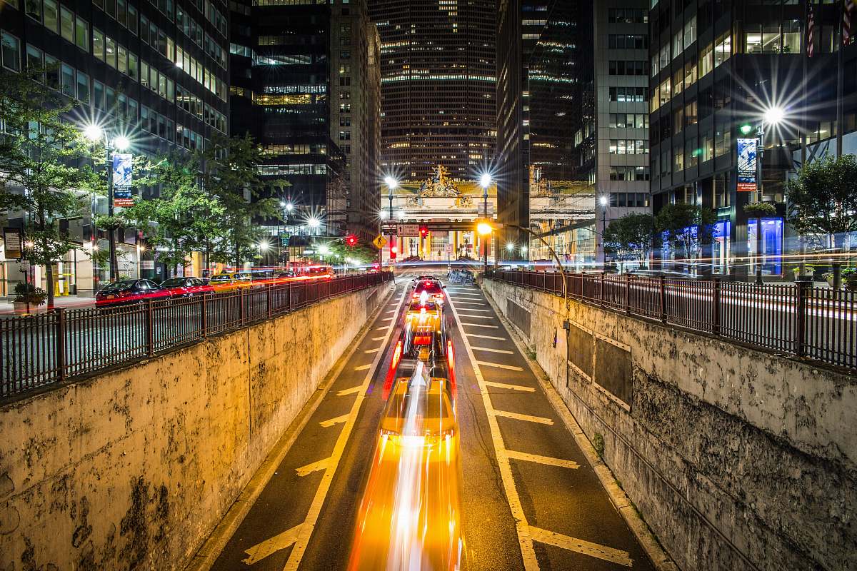 new york time lapse photography of vehicle passing on concrete road surround high-rise buildings during night time urban